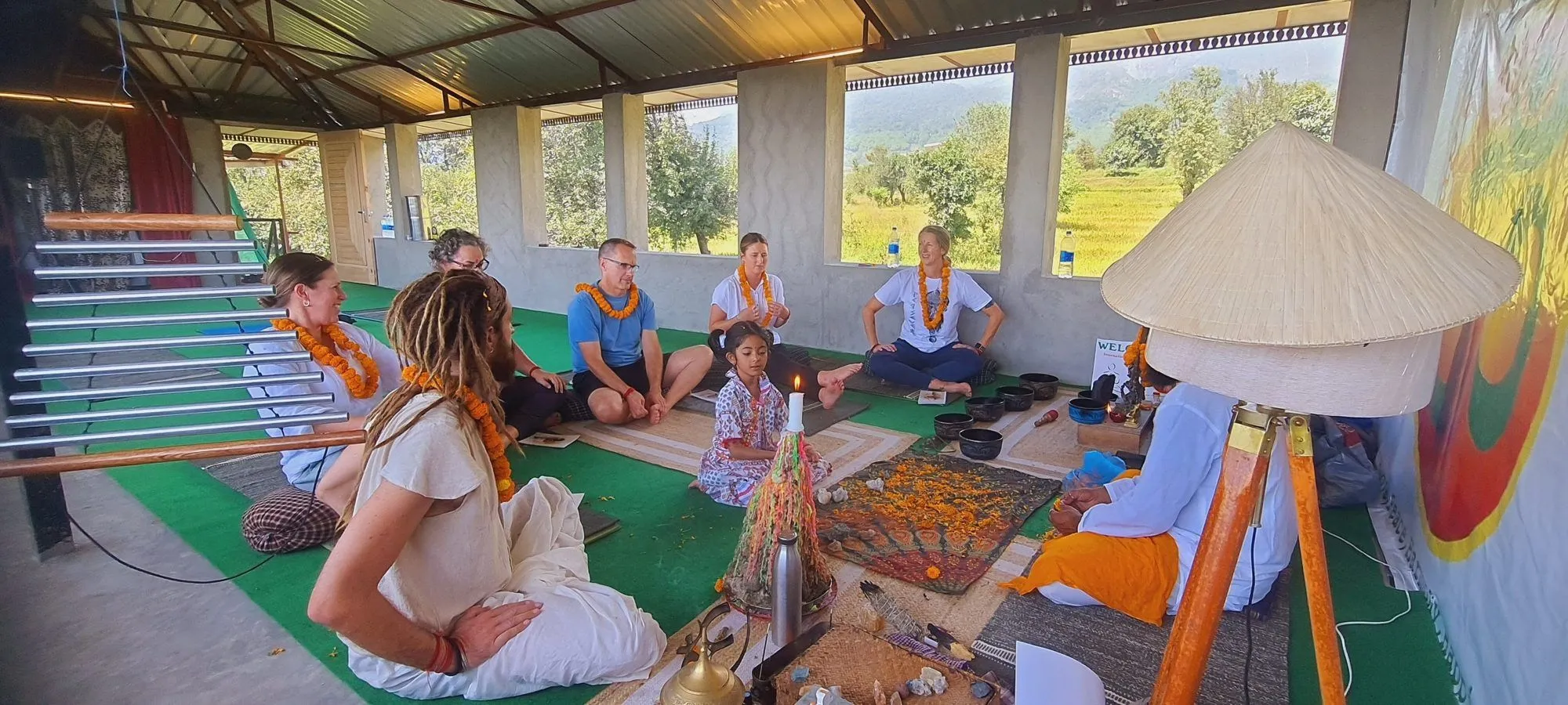 Students sitting on mats in an open-air practice hall with Omji, listening to him teach